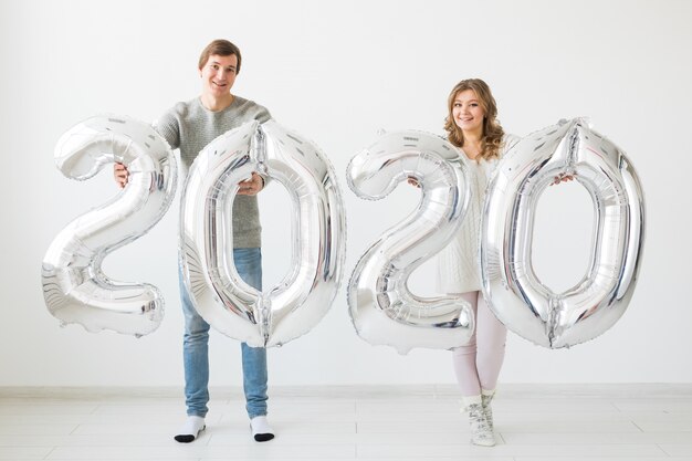 Concept de vacances, de fête et de fête - Un couple d'amoureux heureux détient des ballons d'argent 2020. Célébration du nouvel an