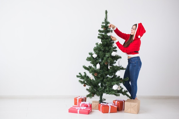 Concept de vacances d'hiver, de Noël et de personnes - Heureuse jeune femme habillée en costume de père Noël décoration de sapin de Noël en blanc la chambre