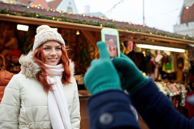 concept de vacances, d'hiver, de noël, de technologie et de personnes - couple heureux de touristes en vêtements chauds prenant un selfie avec un smartphone dans la vieille ville