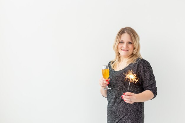 Concept de vacances, Noël, anniversaire et nouvel an - Une femme célèbre et tient du vin dans un verre et un cierge magique sur fond blanc, gros plan