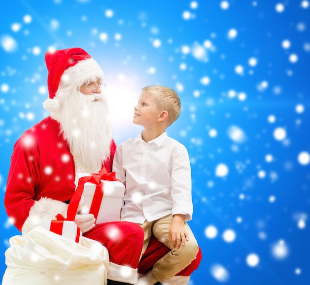 concept de vacances, de noël, d'enfance et de personnes - petit garçon souriant avec le père noël et des cadeaux sur fond de neige bleu