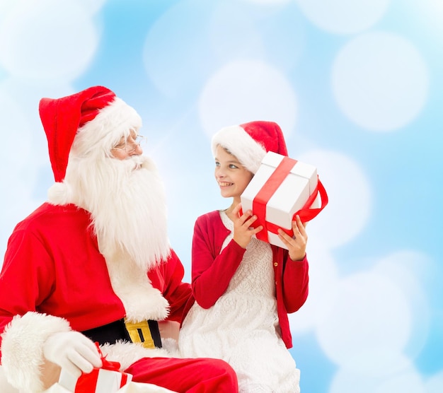 concept de vacances, de noël, d'enfance et de personnes - petite fille souriante avec le père noël et des cadeaux sur fond de lumières bleues