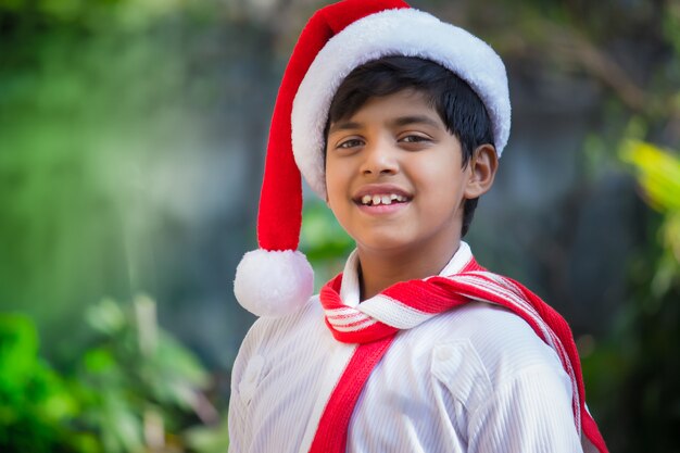 Concept de vacances de Noël Heureux jeune garçon souriant intelligent avec bonnet de père Noël regardant la caméra