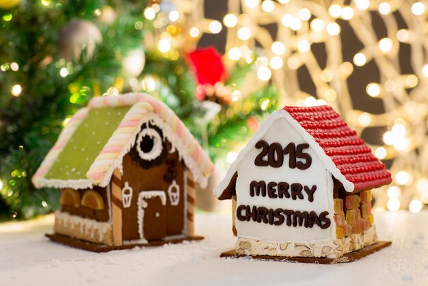 concept de vacances, de noël, de pâtisserie et de bonbons - gros plan de belles maisons en pain d'épice sur table sur fond de lumières