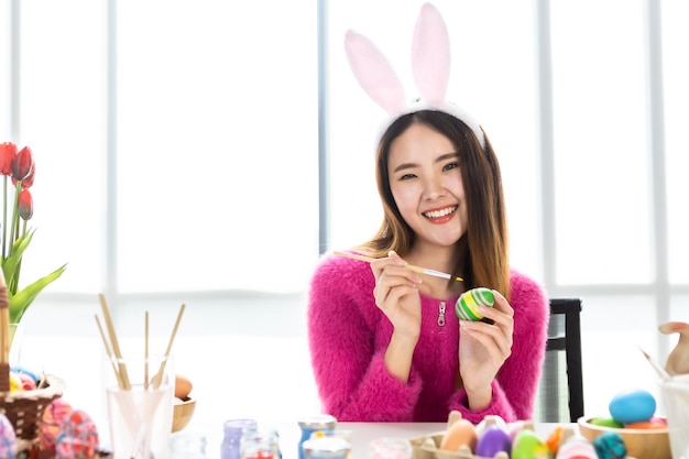 Concept de vacances de Pâques, heureuse jeune femme asiatique portant des oreilles de lapin oeufs peints à la main pour Pâques avec des oeufs de Pâques colorés dans le fond de la salle blanche