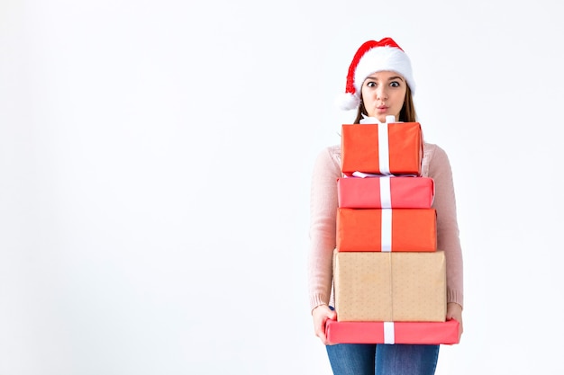 Concept de vacances et de personnes - Noël santa woman shopping tenant de nombreux cadeaux portant un bonnet de noel souriant heureux sur fond blanc avec espace de copie.