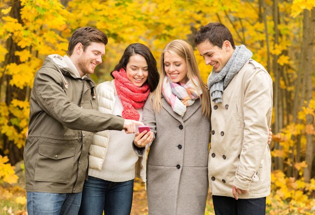 concept de vacances, de personnes, de technologie et d'amitié - groupe d'amis souriants avec smartphone dans le parc d'automne
