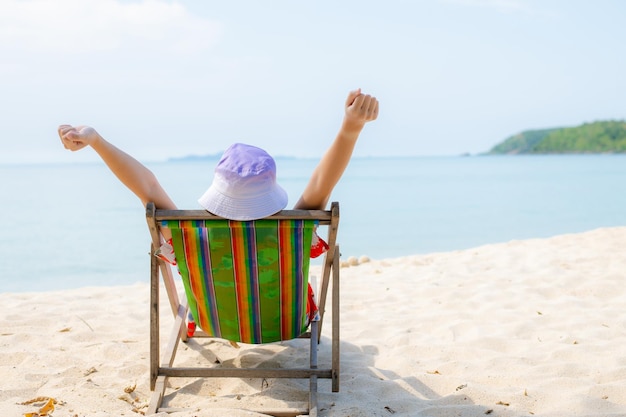 Concept de vacances à la plage d'été Asie femme avec chapeau relaxant et bras levé sur la plage de la chaise en Thaïlande