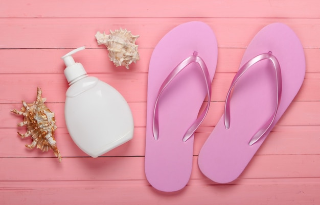 Concept de vacances à la plage, été. Tongs avec bouteille de crème solaire, coquillage sur bois rose