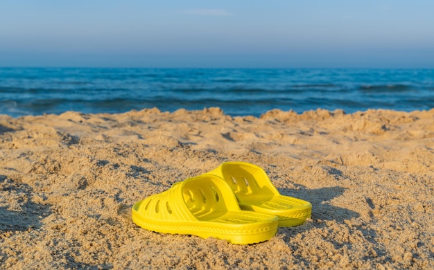 Photo concept de vacances plage pantoufles jaunes sur le sable près de la mer