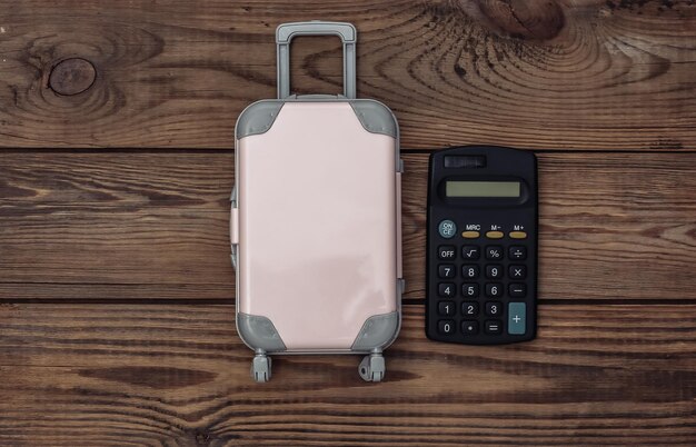 Concept de vacances et de planification de voyage à plat. Mini valise de voyage en plastique et calculatrice sur fond en bois. Vue de dessus