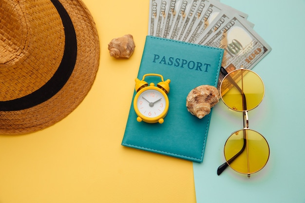 Concept de vacances. Plat simple minimal avec passeport, lunettes de soleil, chapeau et coque sur une surface bleu jaune. Essentiels touristiques