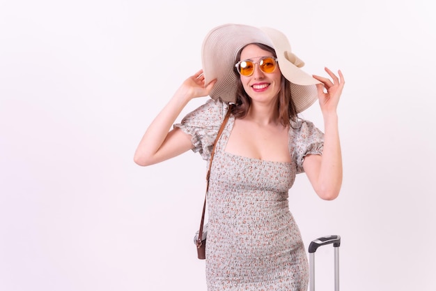 Concept de vacances Portrait d'une jeune femme touristique souriante avec valise et chapeau sur fond blanc