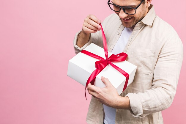 Concept de vacances. Portrait d'un jeune homme ouvrant la boîte-cadeau isolé sur mur rose.