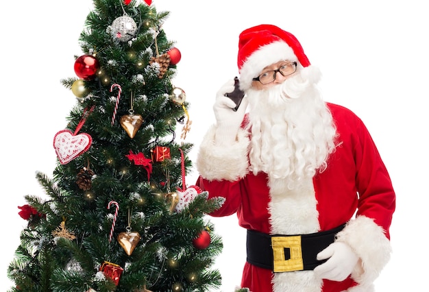 concept de vacances, de technologie et de personnes - homme en costume de père noël avec smartphone et arbre de noël