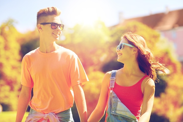 concept de vacances, de vacances, d'amour et de personnes - heureux couple d'adolescents souriants marchant et se regardant dans le parc d'été