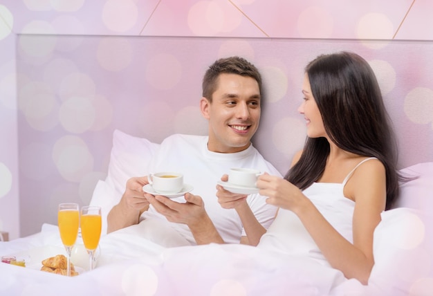 concept de vacances, vacances, personnes, romance et saint valentin - couple heureux prenant son petit déjeuner au lit à l'hôtel ou à la maison sur fond de lumières