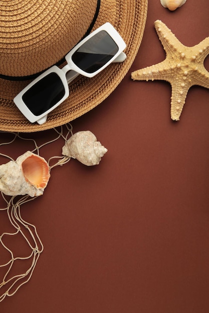 Concept de vacances de voyage Chapeau avec des lunettes de soleil et des coquillages sur fond marron Espace pour le texte Photo verticale