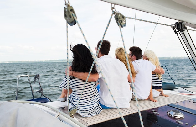 concept de vacances, de voyage, de mer, d'amitié et de personnes - amis heureux naviguant et assis sur un yacht ou un pont de bateau à voile