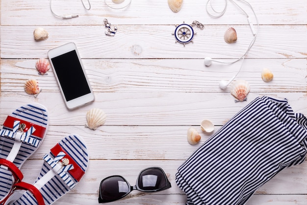 Concept de vacances de voyage avec des sandales, des écouteurs, des lunettes de soleil, un smartphone, des coquillages et un t-shirt rayé.