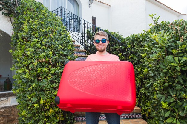 Concept de vacances, de voyage et de tourisme. Bel homme avec valise rouge debout à l'étage.