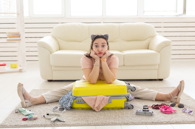 Concept de vacances, de voyage et de voyage - La jeune femme récupère une valise à la maison dans la chambre, beaucoup de choses, des vacances et une valise jaune.