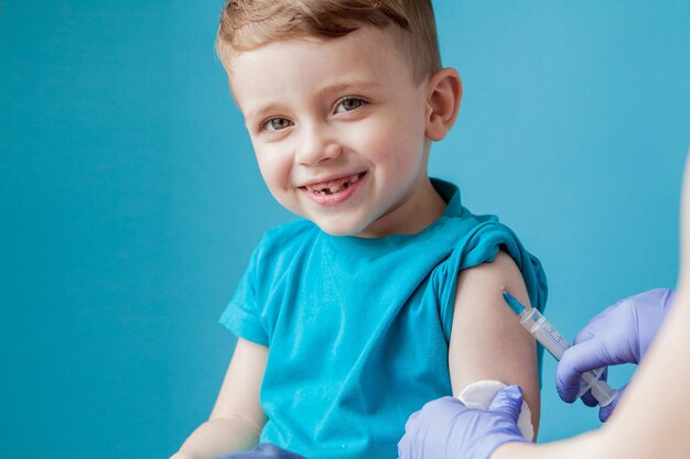 Concept de vaccination Femme médecin vaccinant mignon petit garçon sur fond bleu gros plan