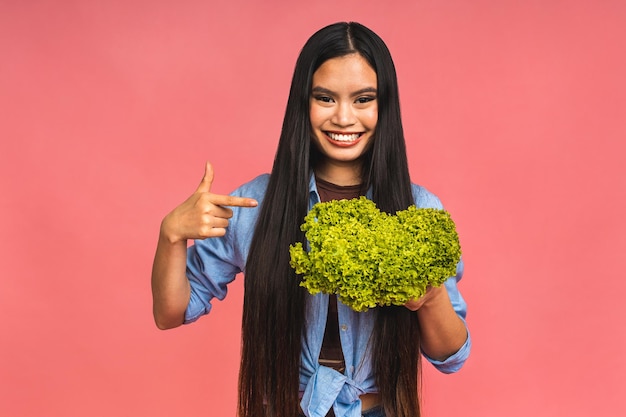 Concept végétarien Femme asiatique heureuse et saine tenant un bol de laitue fraîche isolée sur fond rose