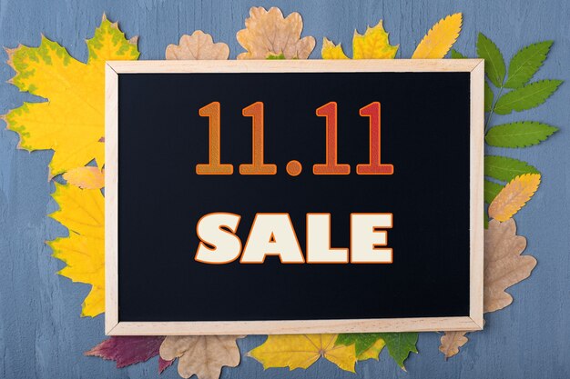 Concept de vente d'automne. Notion de vendredi noir. Date du 11 novembre. Calendrier des soldes d'automne. Cadre noir avec l'inscription 11.11 SALE sur un fond avec des feuilles d'automne sur un fond bleu en bois.