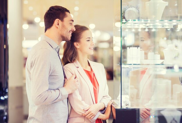 concept de vente, de consommation et de personnes - couple heureux pointant du doigt la vitrine d'une bijouterie dans un centre commercial