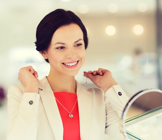 concept de vente, de consommation, de shopping et de personnes - femme heureuse choisissant et essayant un pendentif dans une bijouterie