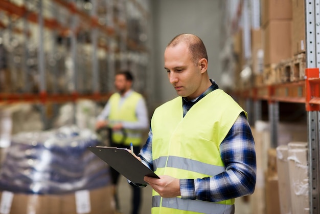 concept de vente en gros, de logistique, de personnes et d'exportation - homme avec presse-papiers dans un gilet de sécurité réfléchissant à l'entrepôt