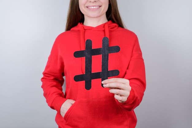 Concept de vente numérique de tweet de site Web de jeunes de marketing. Photo en gros plan recadrée d'un jeune sourire à pleines dents optimiste et joyeux positif tenant un grand gros hashtag noir dans un fond gris isolé de paume