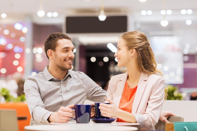 concept de vente, de shopping, de consommation, de loisirs et de personnes - couple heureux avec des sacs à provisions buvant du café dans un centre commercial