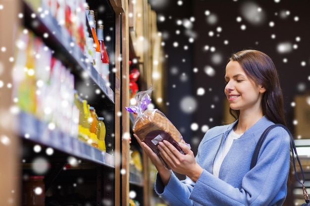 concept de vente, de shopping, de consommation et de personnes - jeune femme heureuse choisissant et achetant du pain sur le marché au-dessus de l'effet de neige