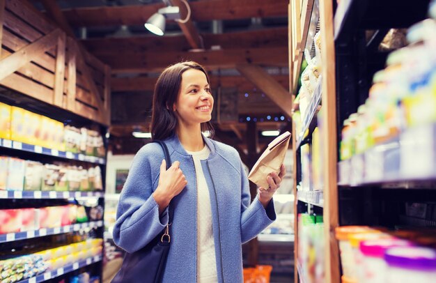 concept de vente, de shopping, de consommation et de personnes - jeune femme heureuse choisissant et achetant de la nourriture sur le marché