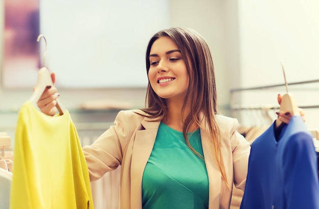 concept de vente, de vêtements, de shopping, de mode et de personnes - jeune femme heureuse choisissant entre une chemise et une veste dans un magasin de vêtements