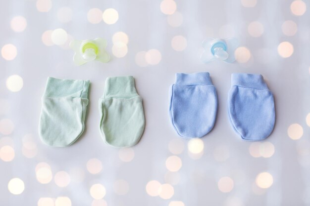 concept de vêtements, de petite enfance, d'accessoires et d'objets - gros plan sur des mitaines et des sucettes pour bébés jumeaux nouveau-nés avec des lumières de vacances