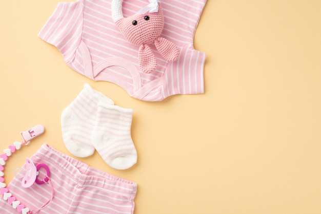 Concept de vêtements pour bébés Vue de dessus photo de chemise rose culotte chaussettes chaîne de sucette et jouet hochet lapin tricoté sur fond beige pastel isolé