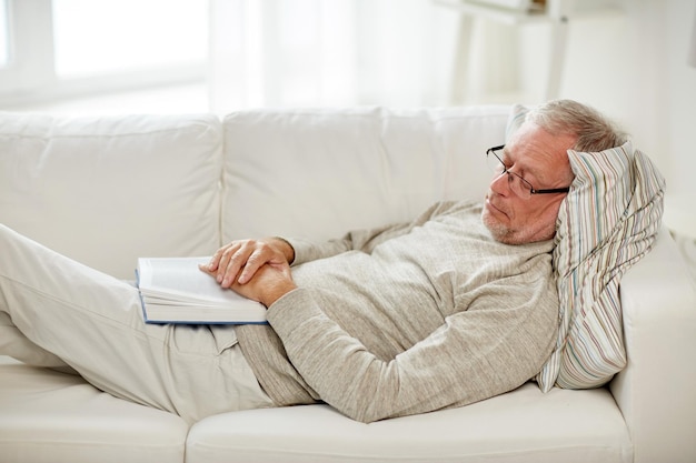 concept de vieillesse, de repos et de personnes - homme âgé allongé sur un canapé avec un livre et dormant à la maison