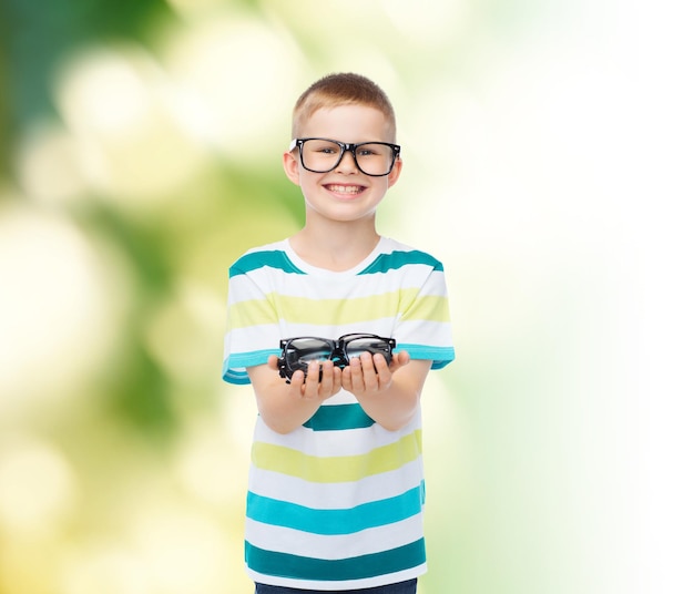 concept de vision, de santé, d'écologie et de personnes - petit garçon souriant dans des lunettes tenant des lunettes sur fond vert