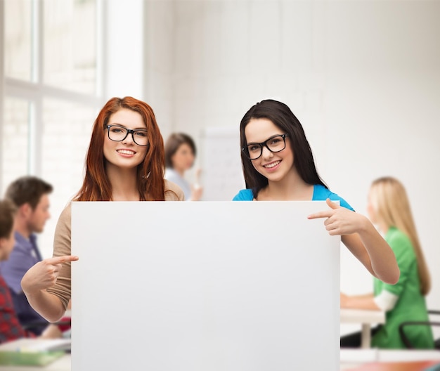 concept de vision, de santé, de publicité et de personnes - deux filles souriantes portant des lunettes pointant du doigt un tableau blanc blanc