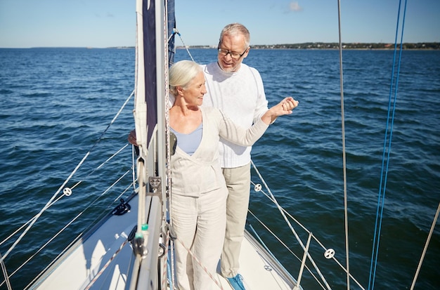 concept de voile, d'âge, de tourisme, de voyage et de personnes - couple de personnes âgées heureux s'embrassant sur un voilier ou un pont de yacht flottant en mer