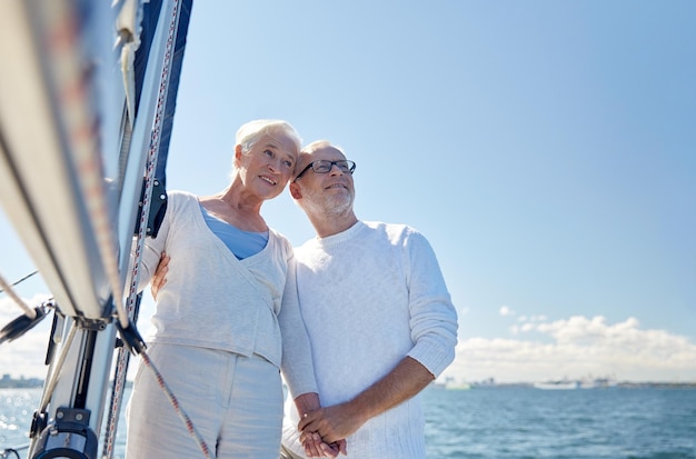 concept de voile, d'âge, de tourisme, de voyage et de personnes - couple de personnes âgées heureux s'embrassant sur un voilier ou un pont de yacht flottant en mer