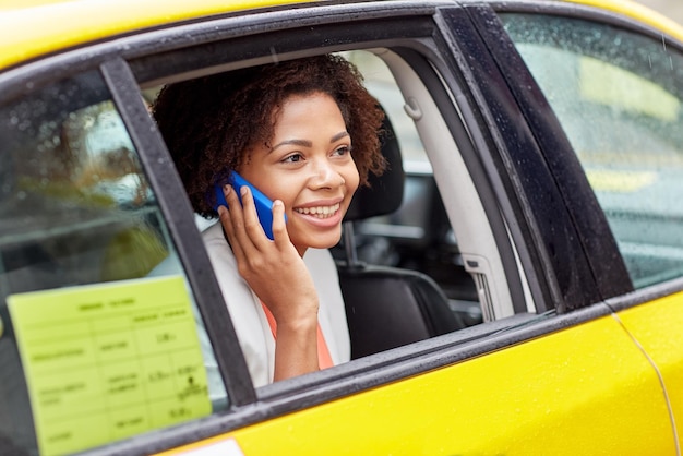 Photo concept de voyage d'affaires, de transport, de voyage, de geste et de personnes - jeune femme afro-américaine souriante appelant sur un smartphone en taxi dans la rue de la ville