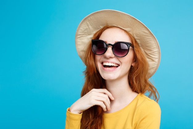 Concept de voyage close up portrait jeune belle fille redhair attrayante avec chapeau à la mode et lunettes de soleil souriant espace copie de mur pastel bleu