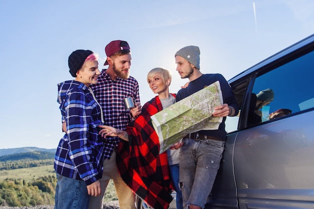 Concept de voyage d'été. Amis heureux à l'aide de la carte papier près de la voiture de location dans la nature.