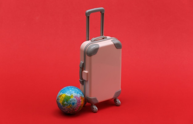 Concept de voyage international. Mini valise de voyage en plastique et globe sur fond rouge. Style minimaliste