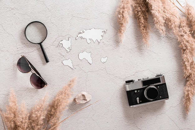 Concept de voyage à plat Continents modèles loupe appareil photo vintage et lunettes de soleil entouré d'herbe sur fond de béton texturé