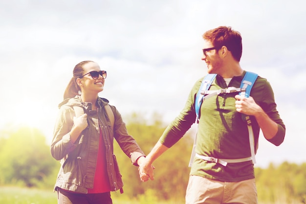 concept de voyage, de randonnée, de randonnée, de tourisme et de personnes - couple heureux avec des sacs à dos se tenant la main et marchant à l'extérieur